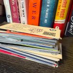 A thick stack of business cards on a desk in front of a shelf of business and marketing books